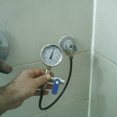 מד לחץ מים מחובר לברז בקיר חדר אמבטיה