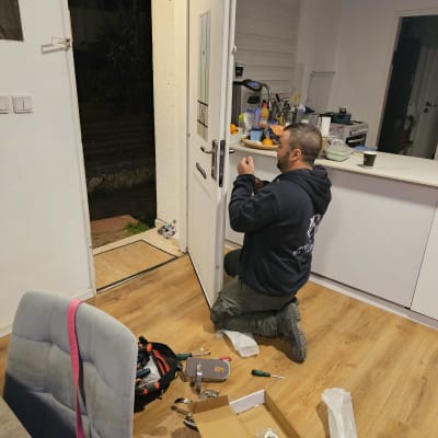 מנעולן מתקין מנעול חדש בדלת כניסה עם כלים על הרצפה
