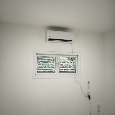 מזגן מותקן על קיר מעל חלון עם תריסים