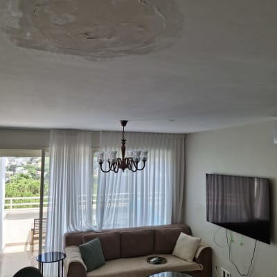 תקרה עם נזק מים, טלוויזיה תלויה, ספה ושולחנות בסלון.