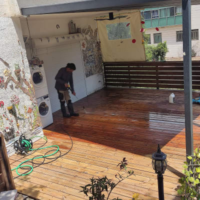 אדם מנקה דק עץ עם צינור מים בגינה