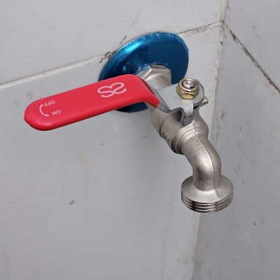 ברז מתכת עם ידית אדומה על קיר לבן