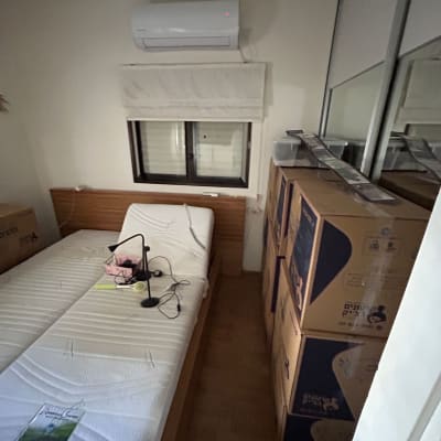 חדר עם מיטה, קופסאות קרטון ומנורת קריאה