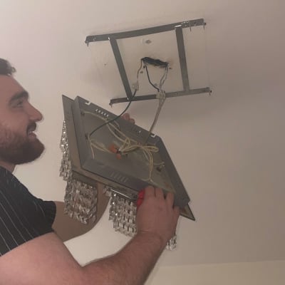 אדם מתקין גוף תאורה בתקרה עם חוטי חשמל