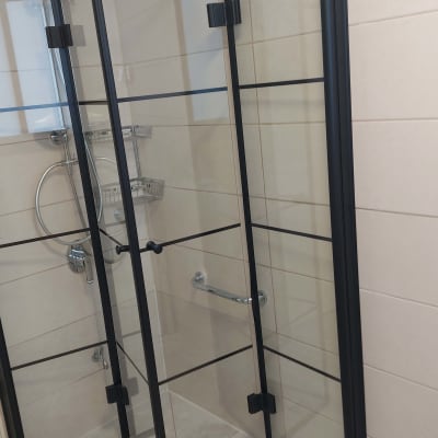 מקלחון זכוכית עם דלתות שחורות ומדף מתכת