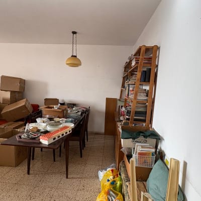 חדר עם קופסאות קרטון, שולחן עם כלים, מדפים עם ספרים