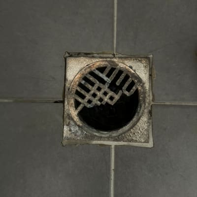 פתח ניקוז מרובע עם רשת מתכת על רצפה אפורה