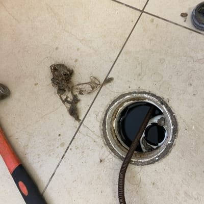 פתח ניקוז עם צינור, פטיש ושערות על הרצפה