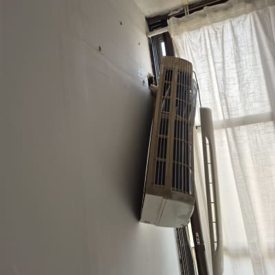 מזגן מותקן על קיר ליד חלון עם וילון לבן