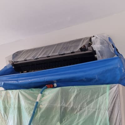 מזגן מכוסה בניילון כחול וירוק עם צינור מחובר