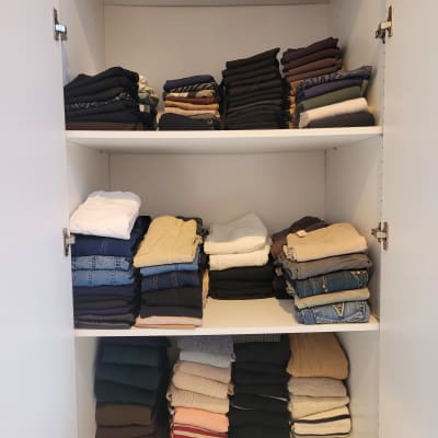 בגדים מקופלים בארון לבן בשלושה מדפים