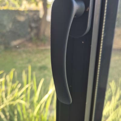 ידית חלון שחורה על רקע גינה ירוקה