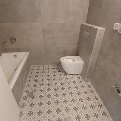 חדר אמבטיה משופץ עם חיפוי קיר אפור, ריצוף מעוטר ואסלה תלויה