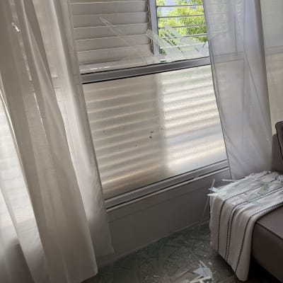 זכוכית שבורה על הרצפה ליד חלון עם וילונות לבנים