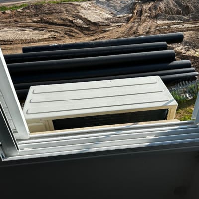 יחידת מזגן חיצונית נראית מחלון פתוח