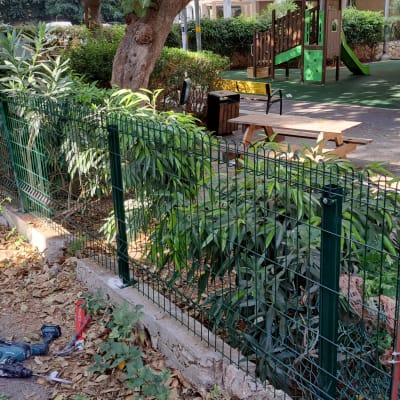 גדר מתכת ירוקה עם צמחים ברקע