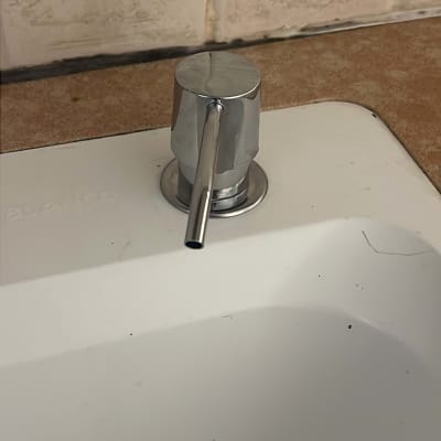 ברז מתכת על כיור לבן עם אריחים ברקע