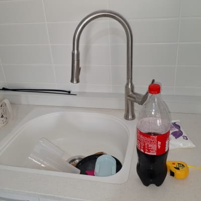 ברז נירוסטה מעל כיור עם כלים ובקבוק קולה על השיש