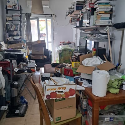 חדר מבולגן עם קופסאות, ספרים וכלי ניקוי על מדפים.