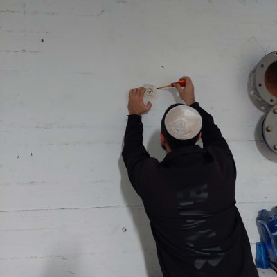 אדם מתקין שקע חשמלי על קיר לבן