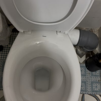 אסלה לבנה עם חיבורי צנרת על רצפה מעוצבת