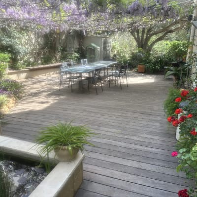 גינה עם דק עץ, שולחן וכיסאות, צמחים ופרחים