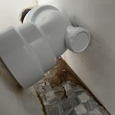 צינור פלסטיק לבן מחובר לקיר עם כתמי חלודה