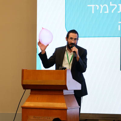 אדם מחזיק בלון ורוד ומדבר במיקרופון