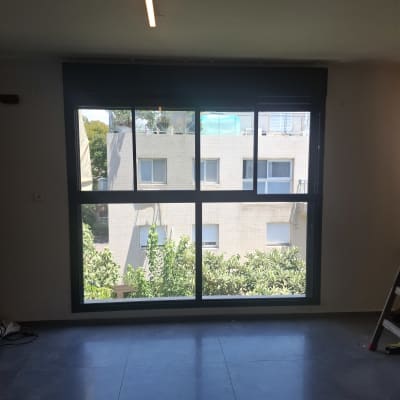 חלון אלומיניום גדול עם נוף לבניין ועצים בחוץ.