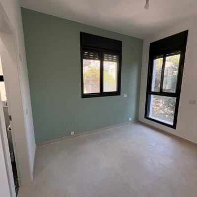חדר ריק עם קיר צבוע ירוק וחלונות גדולים