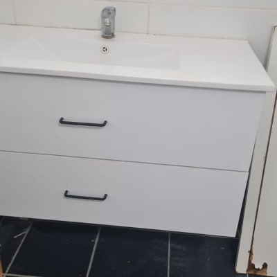 ארון אמבטיה לבן עם ידיות שחורות ודלת עץ פגומה