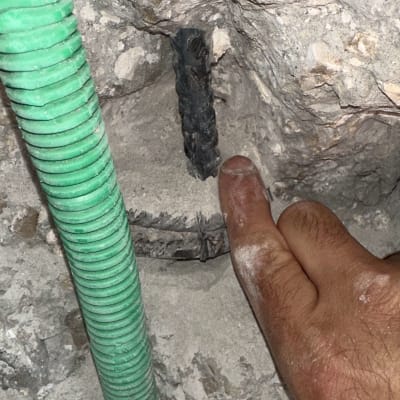 אצבע מצביעה על חוט חשמל בקיר בטון עם צינור ירוק