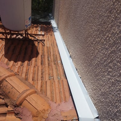 רעפים חומים על גג עם מרזב לבן צמוד לקיר