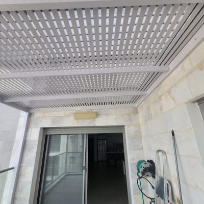 פרגולה מאלומיניום מותקנת במרפסת עם קיר אבן