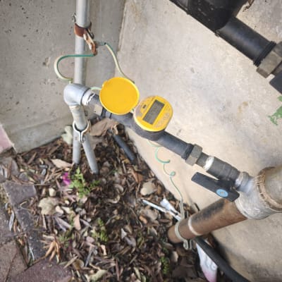 מד מים צהוב מחובר לצינור ליד קיר בטון