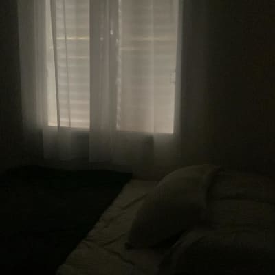 תריסים סגורים מאחורי וילון לבן בחדר חשוך