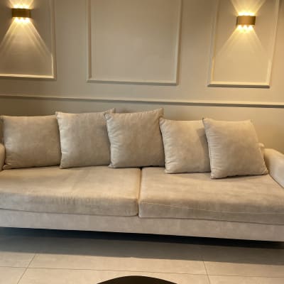 ספה בהירה עם כריות על רקע קיר מעוצב