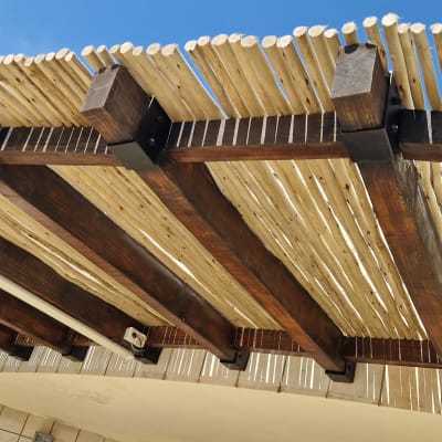 פרגולה מעץ עם קורות במבוק על רקע שמיים כחולים