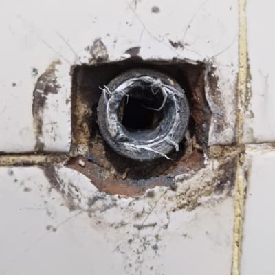 צינור מתכת חשוף בקיר עם אריחים שבורים