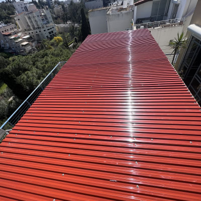 גג מתכת אדום עם ברגים ונוף עירוני ברקע