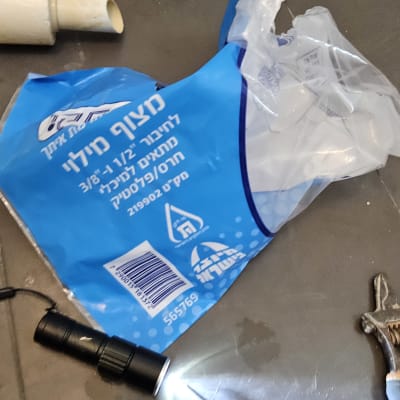 כלי עבודה של אינסטלטור על הרצפה, כולל פנס ומברג.