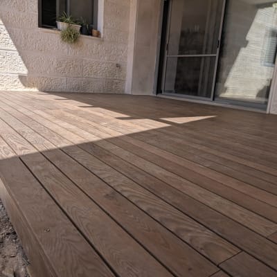 דק עץ מותקן בחצר בית עם קיר אבן