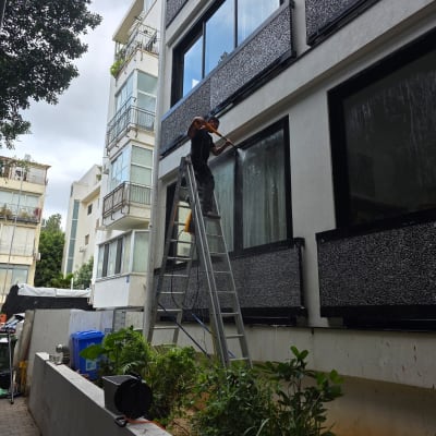 אדם מנקה חלונות של בניין בעזרת סולם וכלי ניקוי