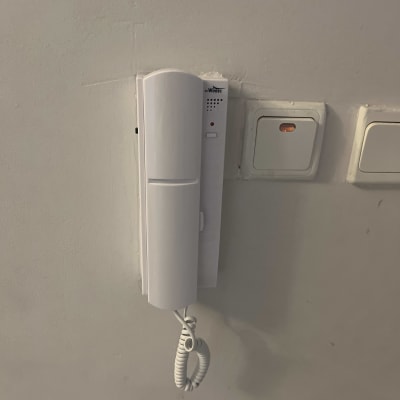 אינטרקום לבן מותקן על קיר עם כבל טלפון