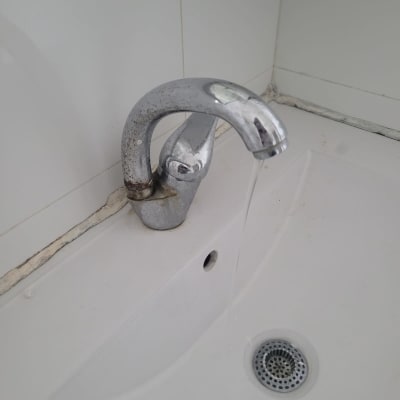 ברז מים מטפטף בכיור לבן עם כתמי חלודה