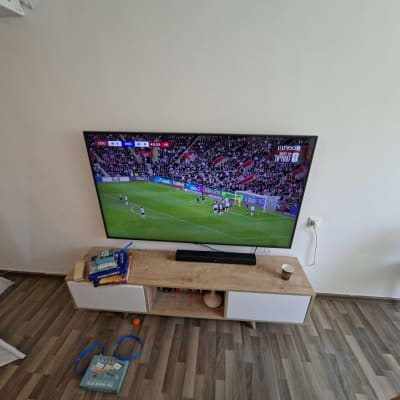 טלוויזיה על קיר עם משחק כדורגל, שולחן קטן וצמח