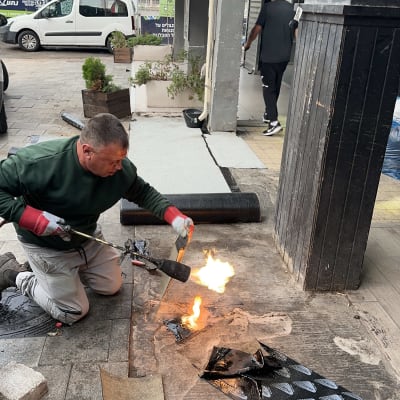 עובד מבצע איטום עם מבער על מדרכה