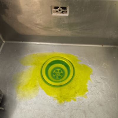 כיור נירוסטה עם כתם נוזל צהוב סביב פתח הניקוז