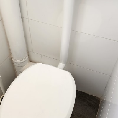 אסלה לבנה עם צינור ניקוז על קיר אריחים