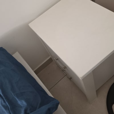 שידה לבנה ליד מיטה עם כרית כחולה